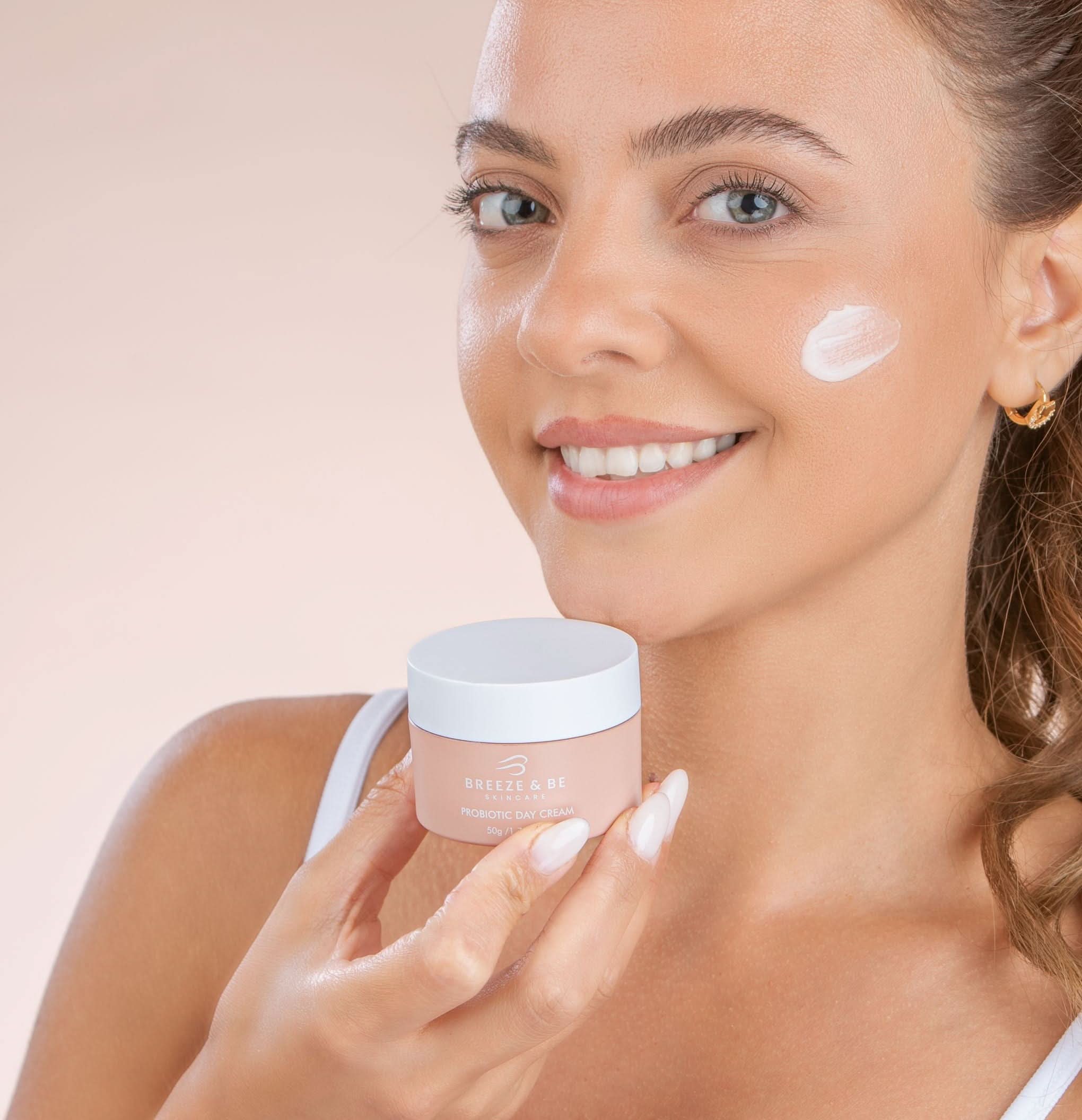 Woman applying cream to her face with a jar of cream in hand on a beige background