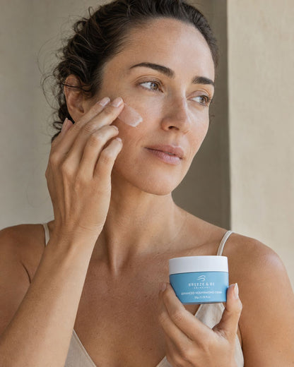 A woman applies a white cream to her cheek while holding a retino cream by Dr. Roy