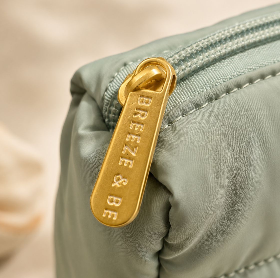 Close-up of the engraved gold Breeze &amp; Be zip pull on the quilted skincare pouch